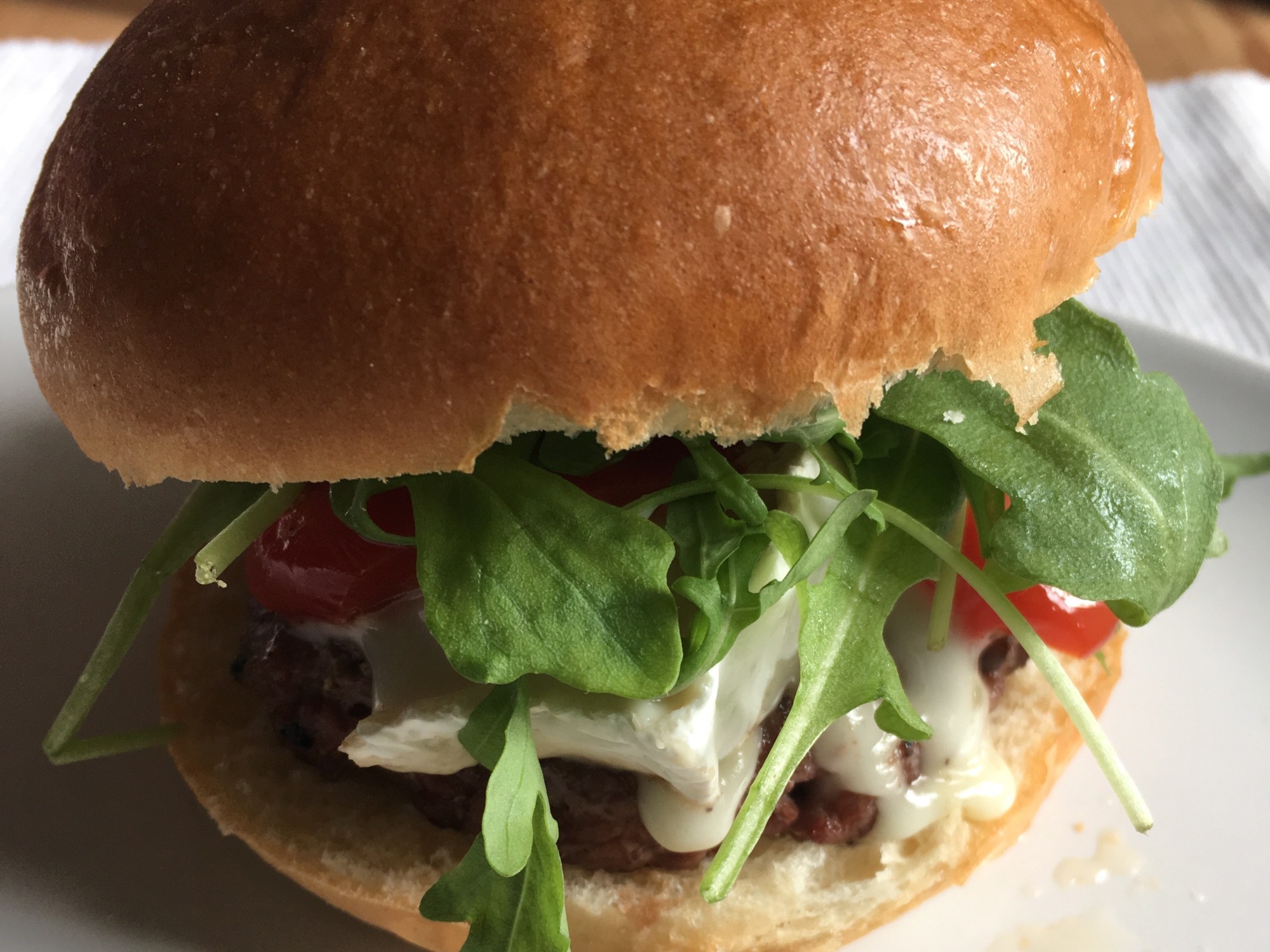 a burger with rocket and melting goat cheese on a brioche bun